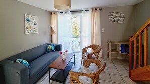 Una sala de estar moderna con un sofá, una mesa de centro, sillas de mimbre, una lámpara de techo y vistas a través de un vidrio.