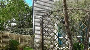 Una casa de madera con valla de celosía, rodeada de un jardín con diversas plantas y flores.