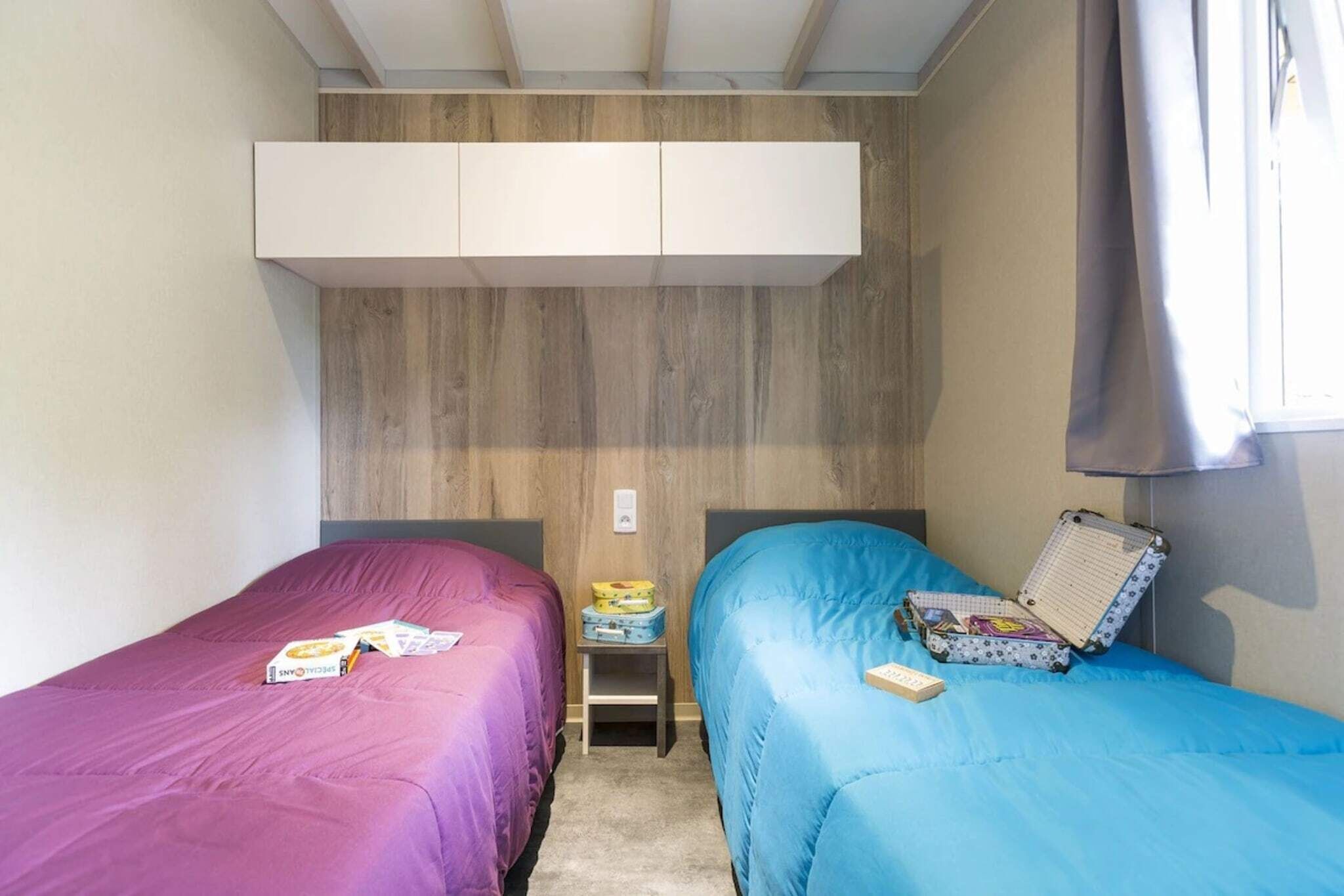Une petite chambre, de taille modeste, comprenant deux lits simples, une petite table et une armoire.