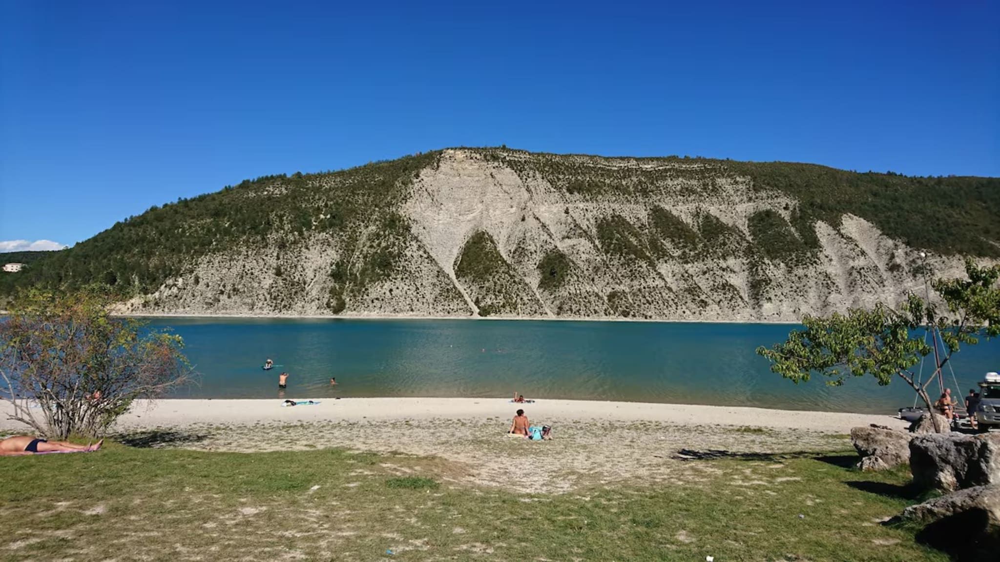 Una spiaggia con vista libera su un lago e una collina sullo sfondo.