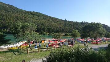 A lakeside campsite with rows of red and blue umbrellas, boats, and a wooden fence.