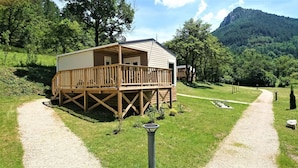 Eine Holzhütte mit einer Veranda, umgeben von einem Kiesweg und üppigem Grün, eingebettet in eine Berglandschaft.