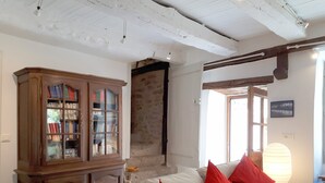 Una sala de estar con un sofá blanco, cojines rojos, un aparador de madera con puertas de cristal y una pared de piedra.