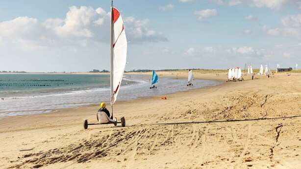 A beach with windsurfing equipment and a sailboat.