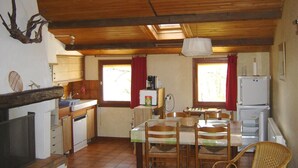 Eine kleine Küche mit Holzbalken, einem Esstisch, Stühlen, einem Kühlschrank und einem Fenster mit Vorhängen.