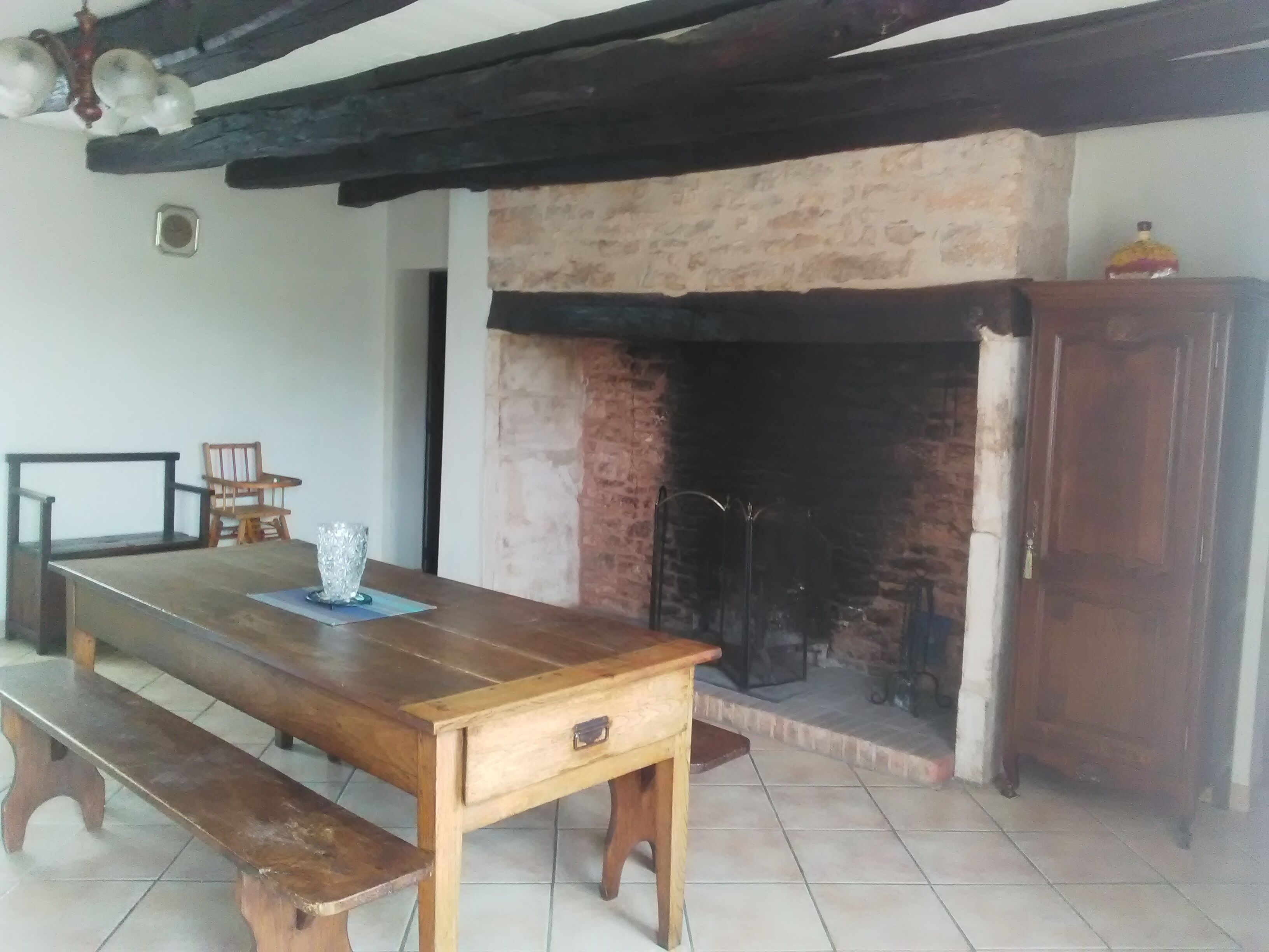 Une pièce rustique avec une table en bois, des bancs, une cheminée et un buffet en bois.