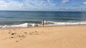 Una playa con huellas que conducen al agua, una persona de pie en la orilla y un cielo despejado.
