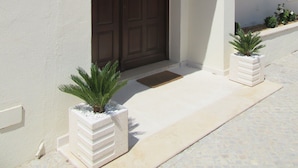 Una entrada estrecha a un edificio con una puerta marrón, un ventanal pequeño y una pared blanca con un borde decorativo.