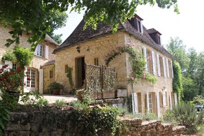 A stone building with a wooden gate, surrounded by greenery and potted plants. - Lovely ancient Périgord house in La Roque-Gageac, close to Sarlat (La Roque-Gageac)
