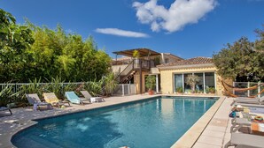 Una piscina con sillones de descanso y una casa al fondo.