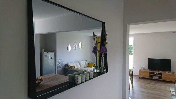 A modern living room with a large mirror, a sofa, a coffee table with decorative items, a television, and a wooden cabinet.