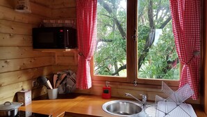 Une cuisine avec un intérieur en bois, un évier en acier inoxydable, un four à micro-ondes et une fenêtre ornée de rideaux à carreaux rouges.