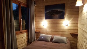 Une pièce chaleureuse, aménagée dans un chalet en bois, avec un lit, deux lampes fixées au mur et une affiche représentant une planète.