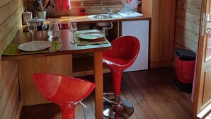Une cuisine compacte aux murs en bois, une fenêtre avec des rideaux rouges, un four à micro-ondes, un évier et un petit réfrigérateur.