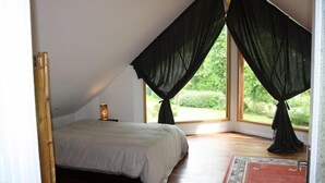 Une chambre avec un plafond en pente, un lit et une grande fenêtre avec des rideaux noirs.