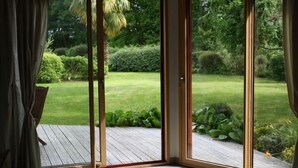 Une pièce dotée d’une porte-fenêtre coulissante donnant sur une terrasse en bois et un jardin.
