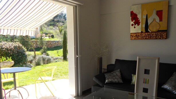 Uma sala de estar moderna com uma mesa de centro de vidro, um sofá preto com almofadas estampadas e um quadro na parede.