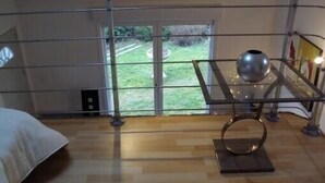 Um quarto com uma cama, uma mesa de vidro com um vaso e vista para o exterior.