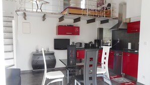 Uma cozinha compacta com armários vermelhos, bancada preta e um espaço de jantar com mesa e cadeiras de vidro.