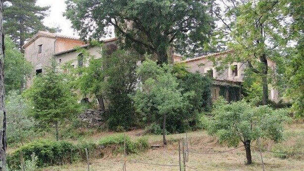 Un bâtiment rustique entouré d’arbres et délimité par une clôture.