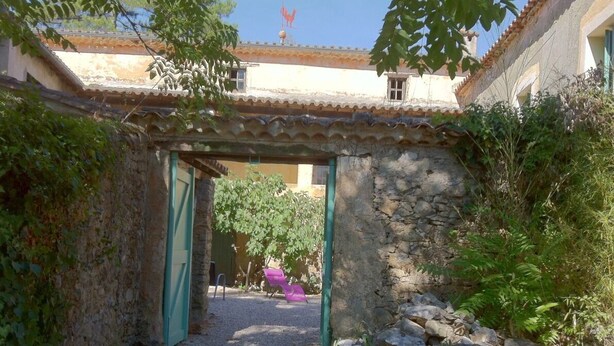 Un patio con un muro de piedra, una puerta verde y una silla rosa.