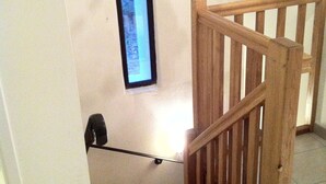 Una escalera de madera con barandilla, una luz de pared y un cuadro enmarco.
