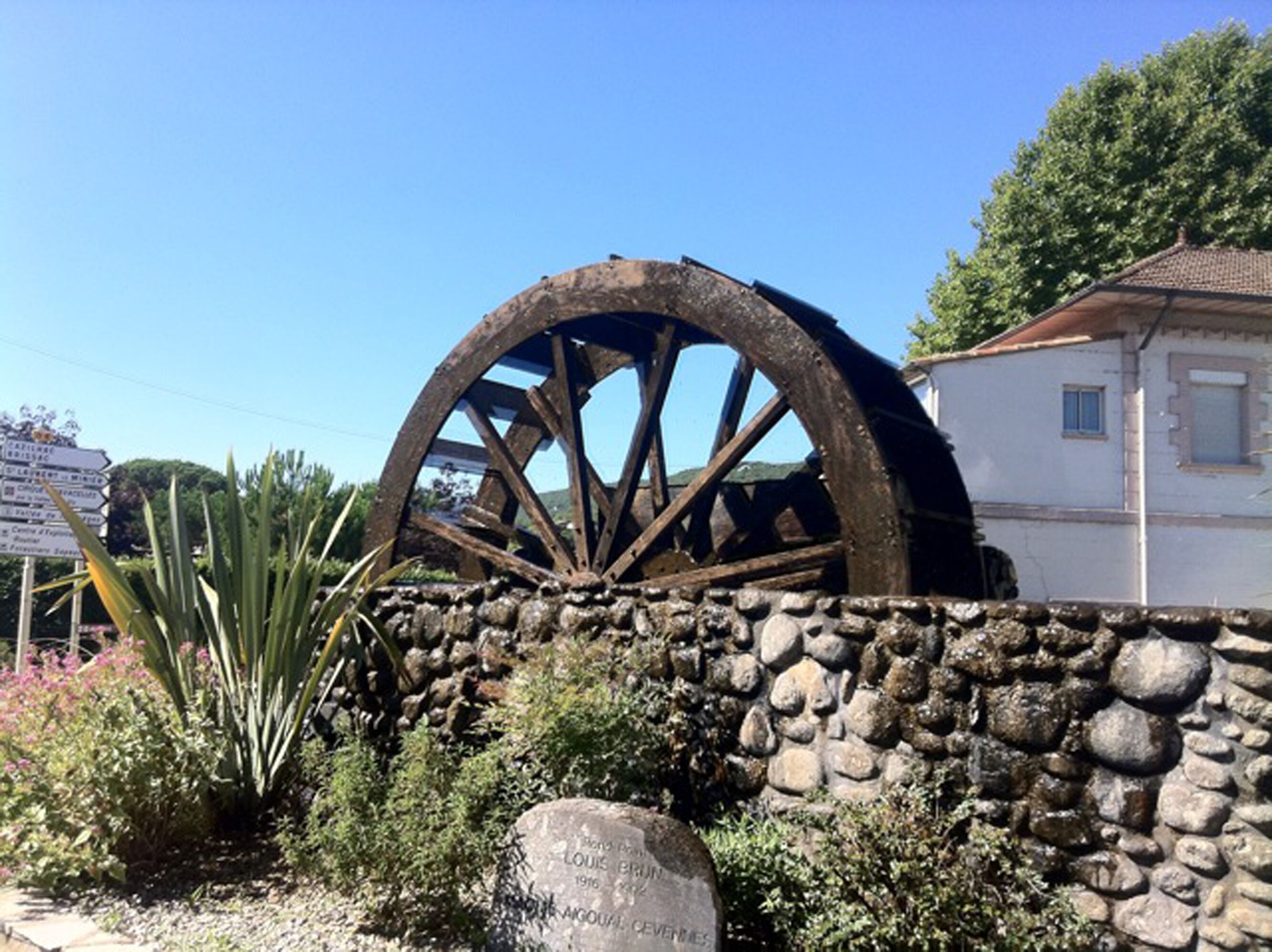 A large wooden water wheel, a stone wall, and a building with a tiled roof.