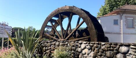 A large wooden water wheel, a stone wall, and a building with a tiled roof.