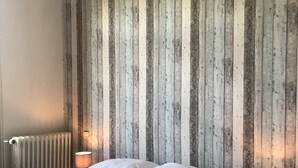 A bedroom with a bed, two bedside lamps, a radiator, and a wooden wall panel. - Gîte in the Bay of Somme (Pendé)