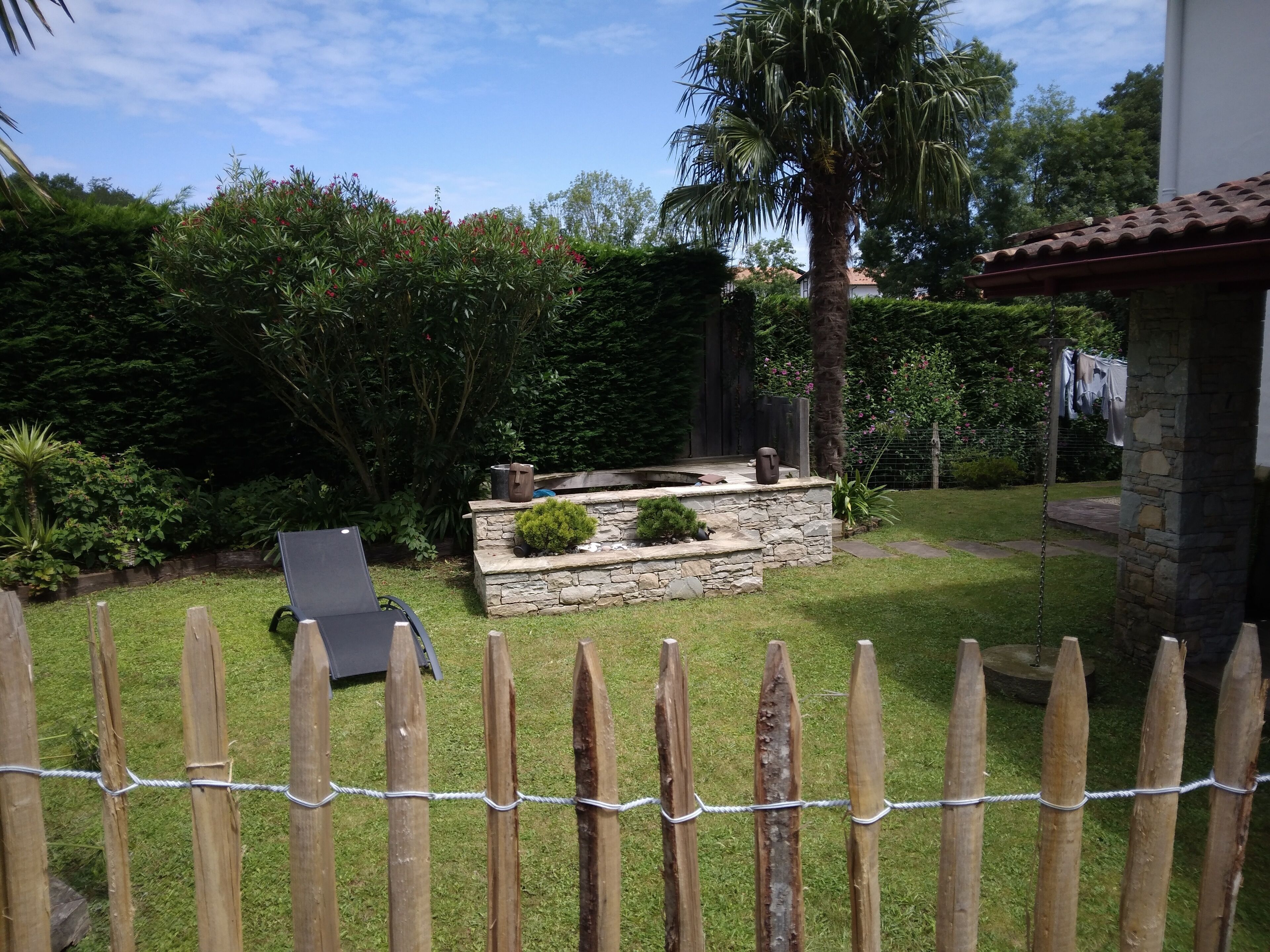 Un patio con muro de piedra, una palmera y una valla de madera.
