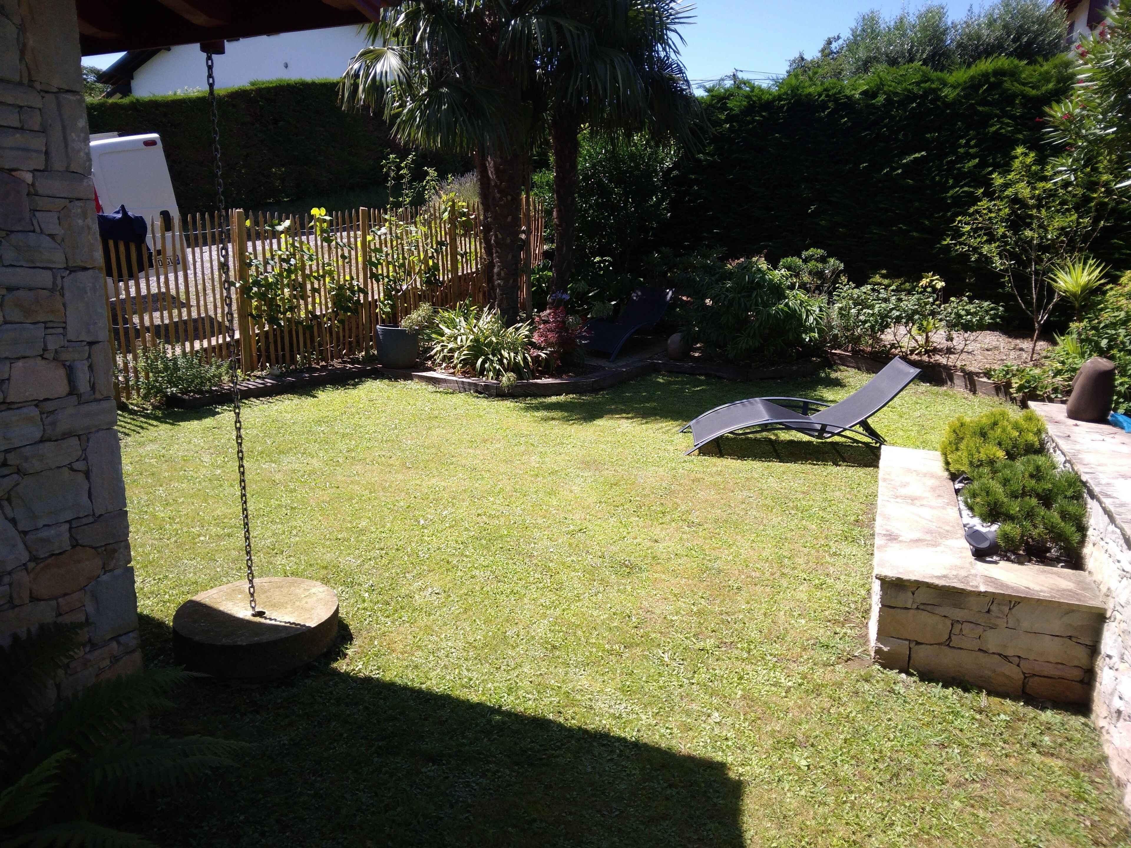 A backyard with a swing set, a lawn chair, and a stone wall.