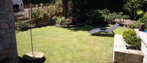 A backyard with a swing set, a lawn chair, and a stone wall.