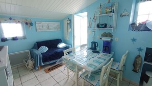 A cozy room with a blue sofa, a dining table with chairs, a coffee maker, and a radiator.