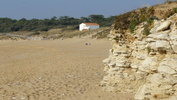 A sandy beach with a white building and a stone wall.