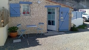 A stone building with a blue door and window shutters, a small table with chairs, and a potted plant.