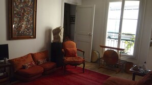 A living room with a red sofa, a patterned armchair, a statue, and a large window with a view of a balcony. - quiet and refined apartment (Paris)