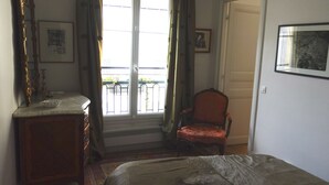 A room with a bed, a chair, a dresser, a window with curtains, and a door. - quiet and refined apartment (Paris)