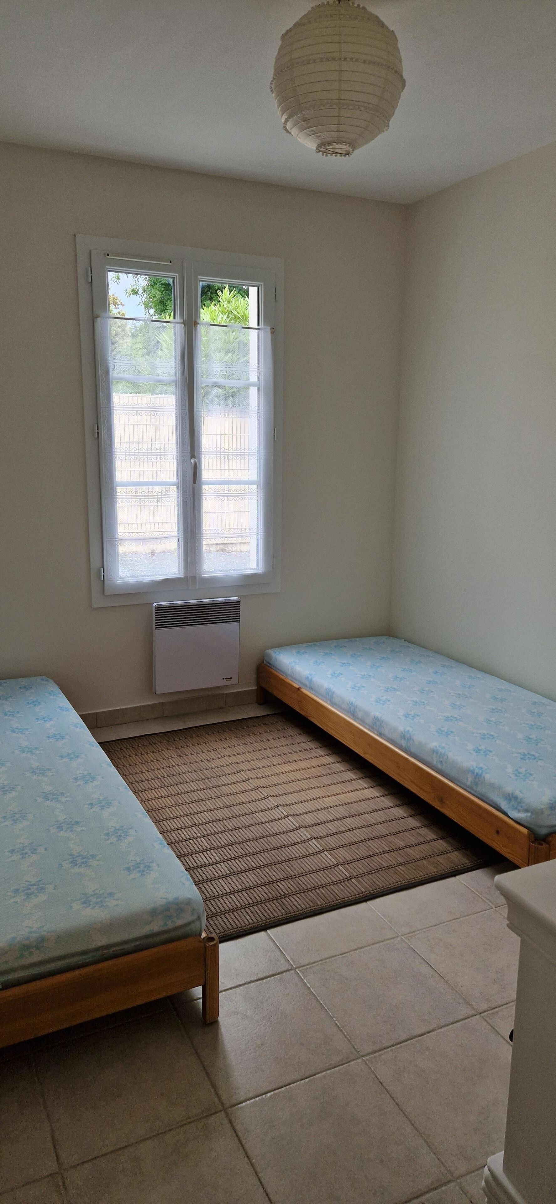 A small room with two single beds, a window with a view, and a ceiling light fixture.