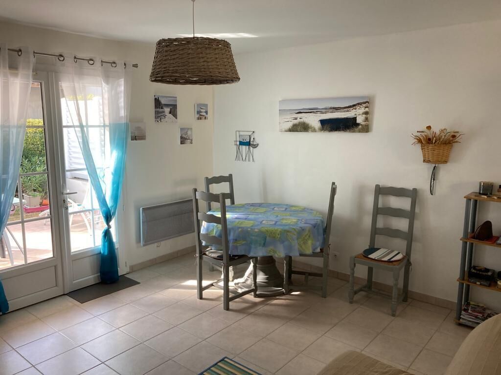 Un espace repas comprenant une table et des chaises, un luminaire suspendu et une vue sur l’extérieur grâce à une porte vitrée.
