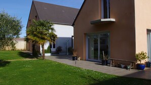 A modern house with a large patio, a palm tree, and several potted plants. - Seaside guest room 1 (Portbail)
