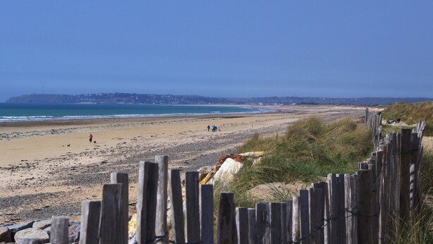 A beach with a wooden fence in the foreground, a sandy shore, and a distant view of a town. - Seaside guest room 1 (Portbail)
