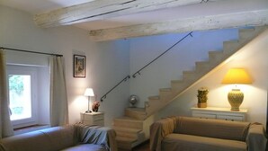 A cozy living room with two sofas, a wooden coffee table, a staircase with a lamp, and a window with curtains.