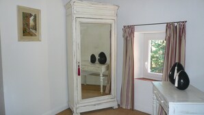 A room with a white wardrobe, a small desk, and a window with curtains.
