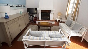 Un salon avec un canapé, des fauteuils, une cheminée, un téléviseur et un tableau accroché au mur.