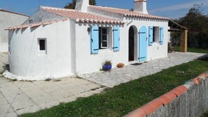 Un petit bâtiment blanc, avec des volets bleus et un toit recouvert de tuiles.