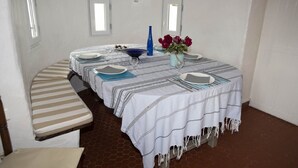 Une pièce comprenant une table de salle à manger ronde, dressée pour quatre personnes, deux bancs, une petite fenêtre et une porte.