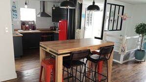 Cozinha com mesa de madeira, cadeiras pretas, geladeira vermelha e luminárias pendentes.