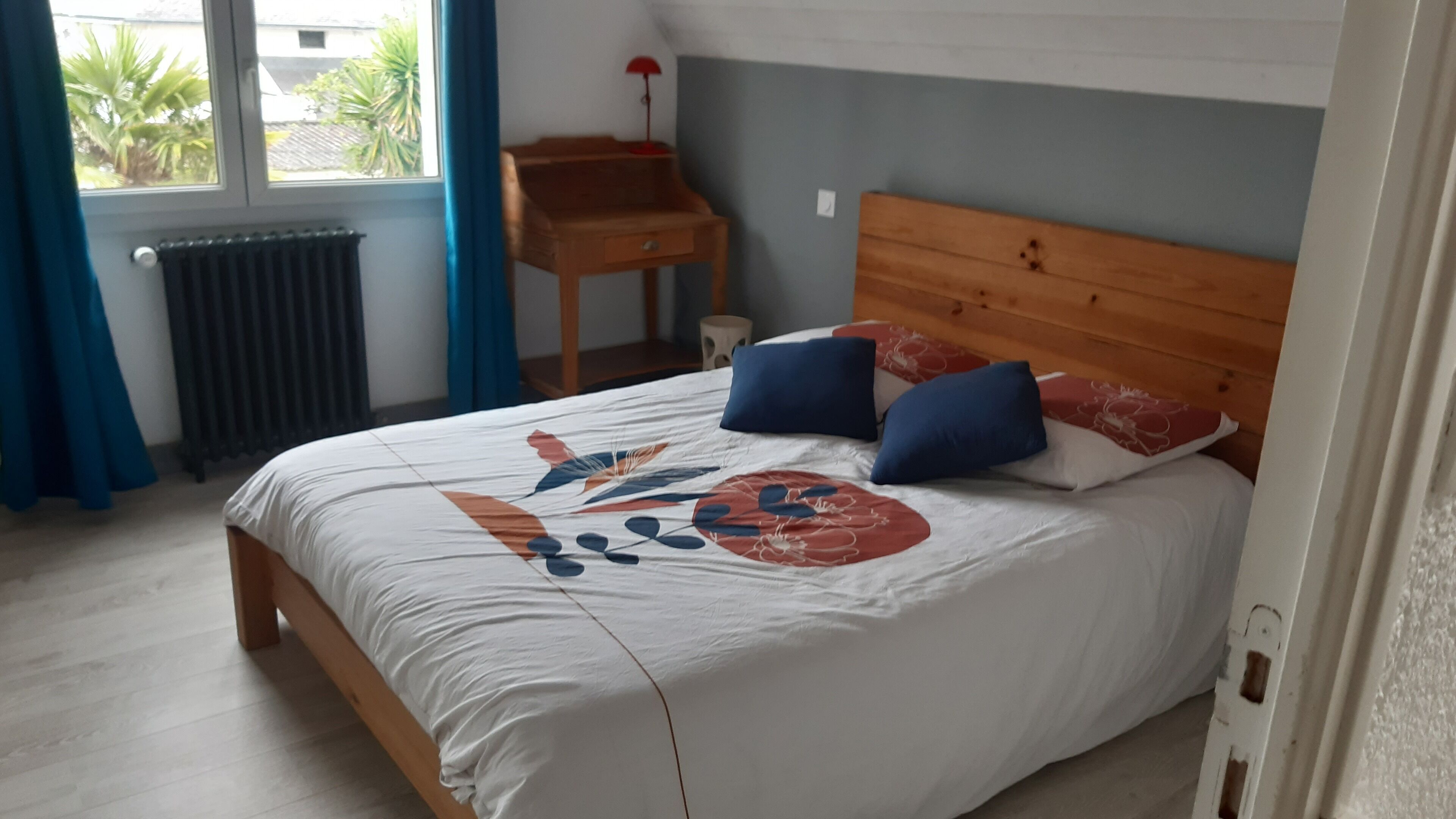 Une chambre à coucher avec un lit en bois, une petite table de chevet en bois, un radiateur et une fenêtre avec des rideaux.