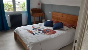 Une chambre à coucher avec un lit en bois, une petite table de chevet en bois, un radiateur et une fenêtre avec des rideaux.