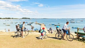 Uma área costeira com bicicletas estacionadas na praia, uma faixa de areia e vista para o mar com muitos barcos.